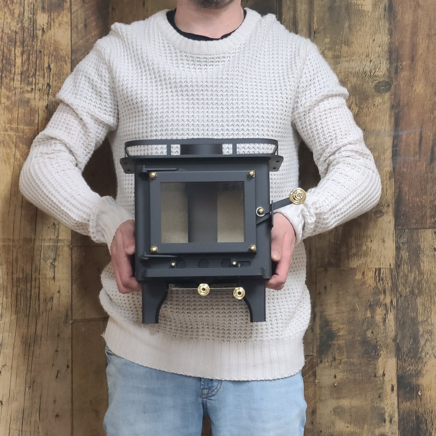 CB-1008 black mini wood stove with a visible firebox and controls, 'Certified' and indicating it meets UL 1482-2022 and ULC S627-2023 standards. held in arms