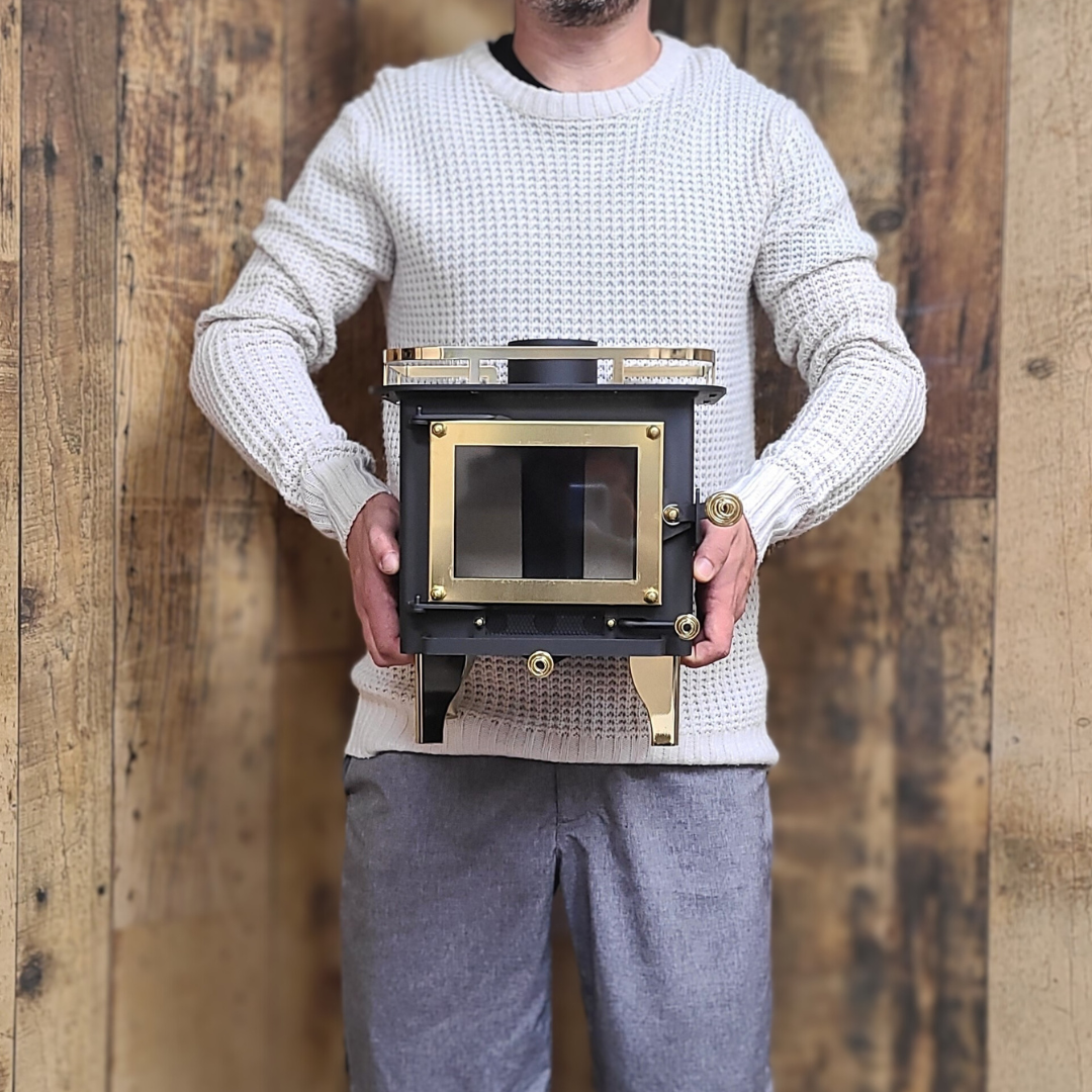 CB-1000 brass wood stove with brass plated coil handles and a visible firebox. Held in arms